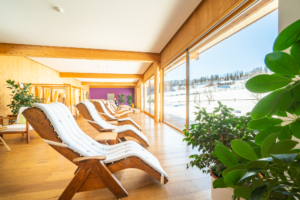 Heller Ruheraum im Biovitalhotel Sommerau mit Holzliegen, großen Panoramafenstern und Blick auf eine verschneite Landschaft.
